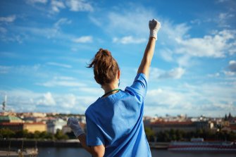 Nurse facing a city with their fist raised high against a blue sky