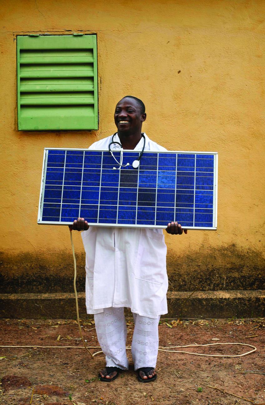 Doctor from Mali holds a solar panel. He is wearing his scrubs and his stethoscope. 